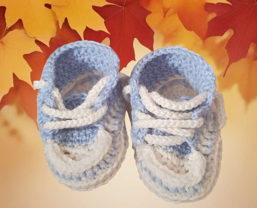Hand-crocheted baby booties in blue and white wool on autumn leaves background