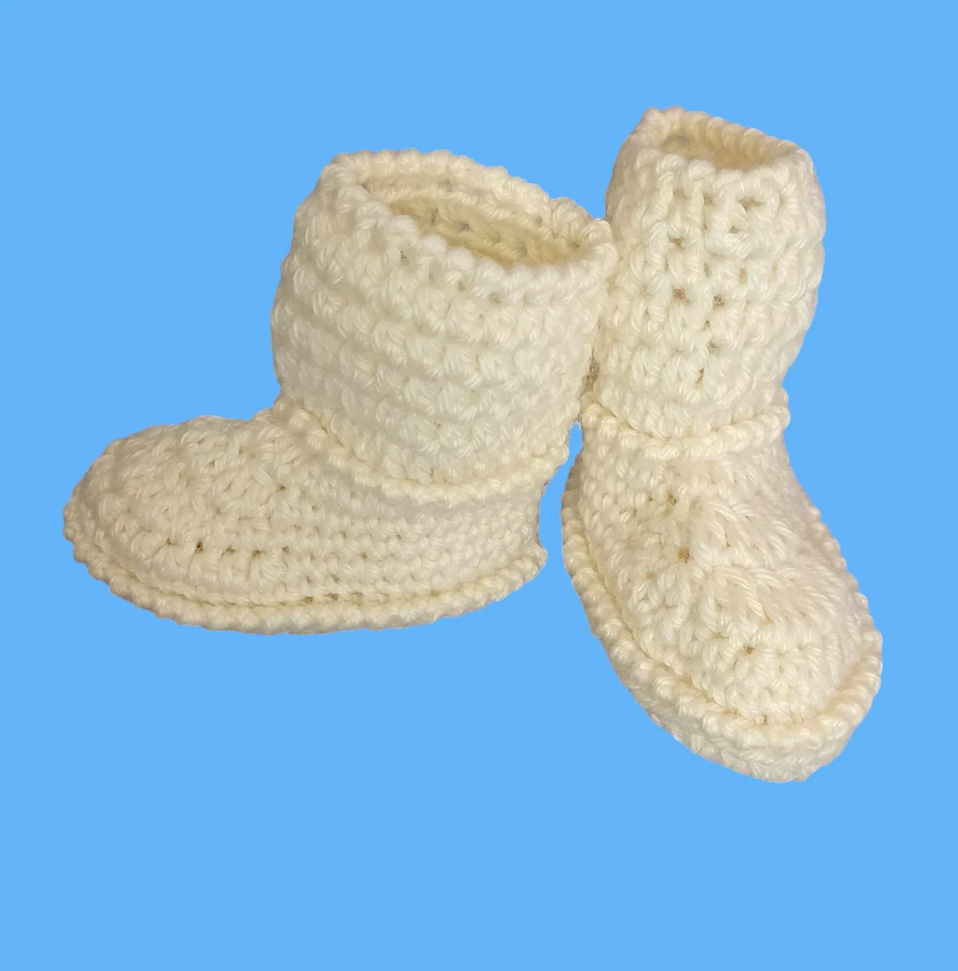 Handmade crochet baby booties in cream yarn by Croch'pelotes, on blue background