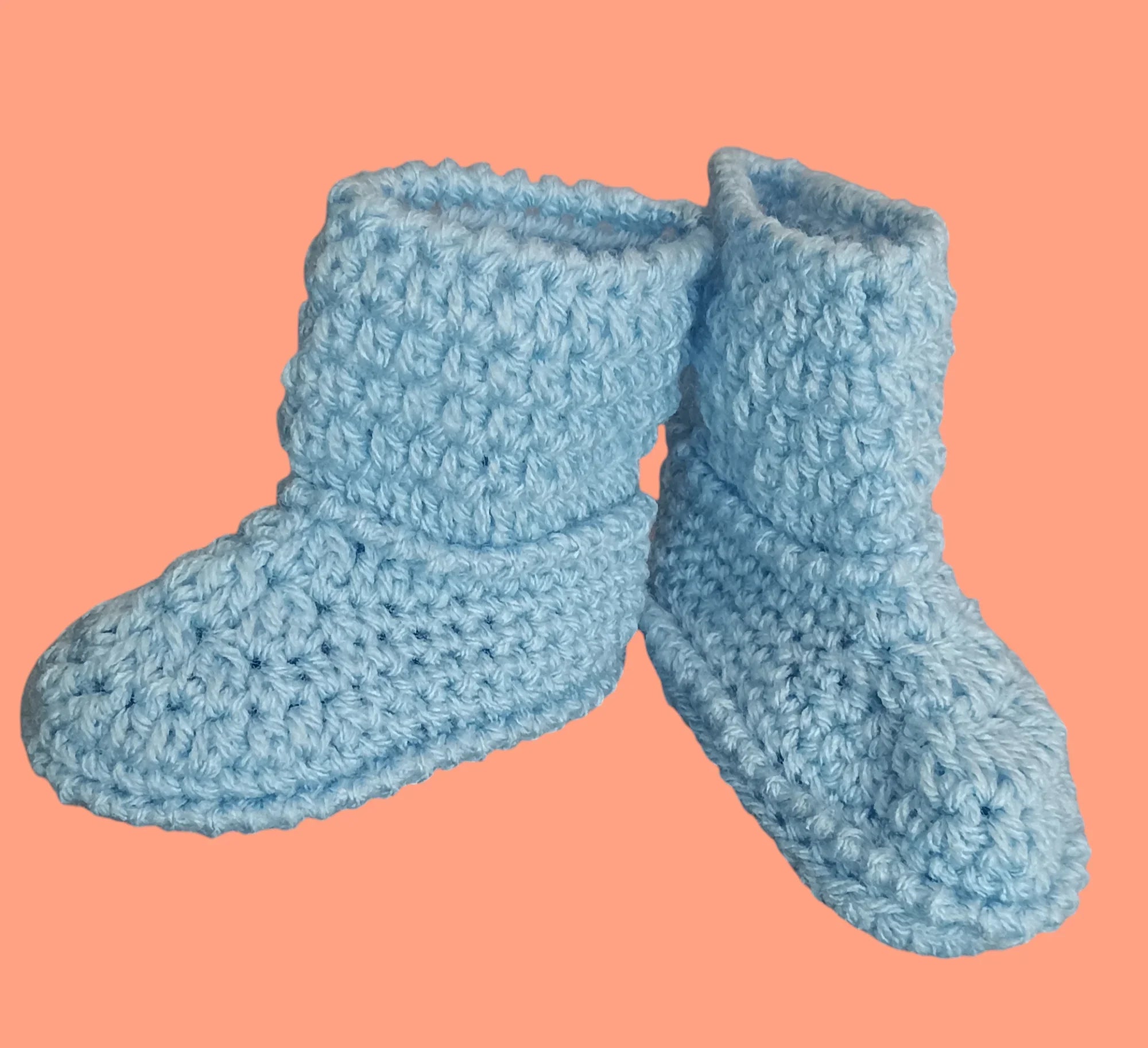 Handmade blue crochet baby booties from Croch'pelotes by Sophie on peach background