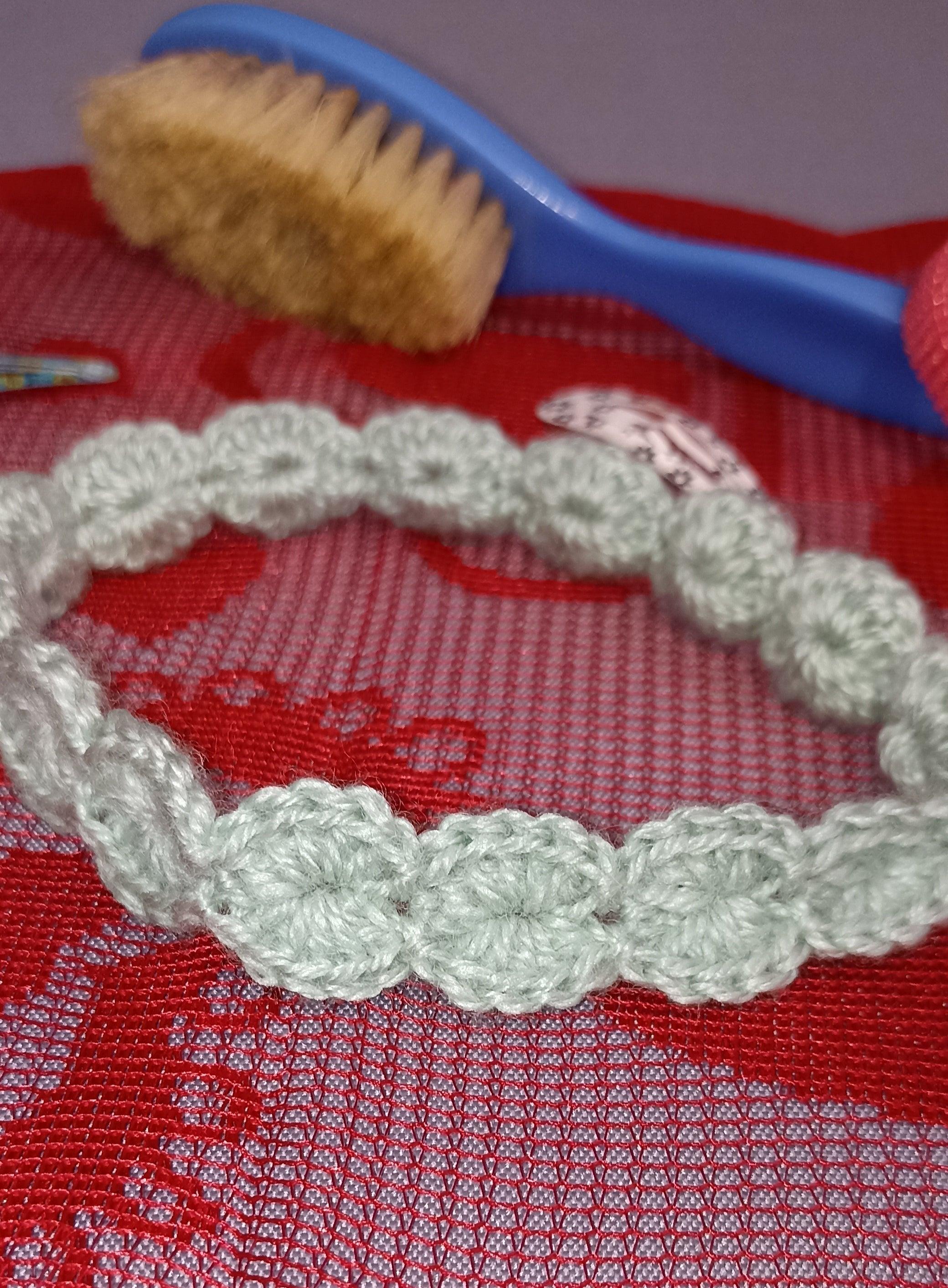 Handmade crochet wool headband in light green, displayed on red fabric near a baby brush