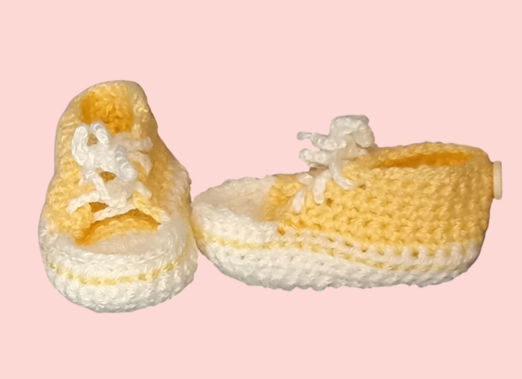 Handmade yellow and white crochet baby booties on a pink background by Croch'pelotes by Sophie